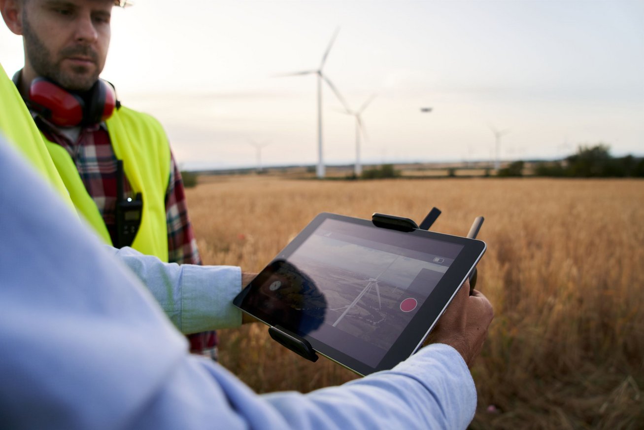 Mænd på mark med vindmøller. Tablet viser dronefilm af vindmøller. Colourbox, #308312.